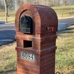 A red brick mailbox is sitting next to a road.