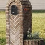 A brick mailbox is sitting in the grass in front of a house.