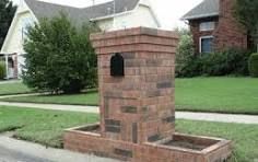 A brick mailbox is sitting on the side of the road in front of a house.
