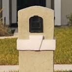 A mailbox is sitting in the grass in front of a house.