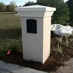 A white mailbox is sitting on a brick sidewalk next to a grassy field.
