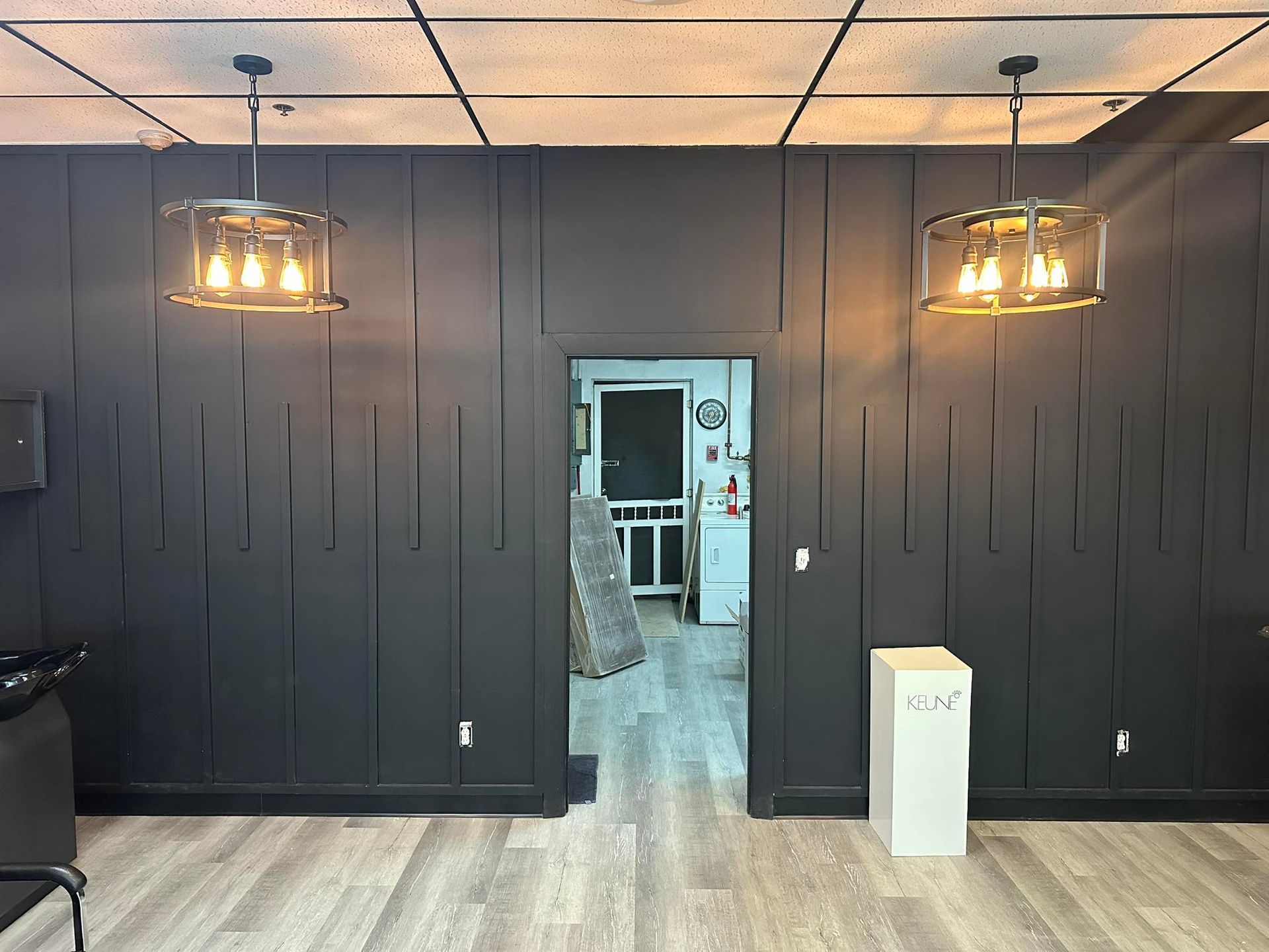 A black accent wall with vertical wood molding, featuring two industrial-style pendant lights and a center doorway.