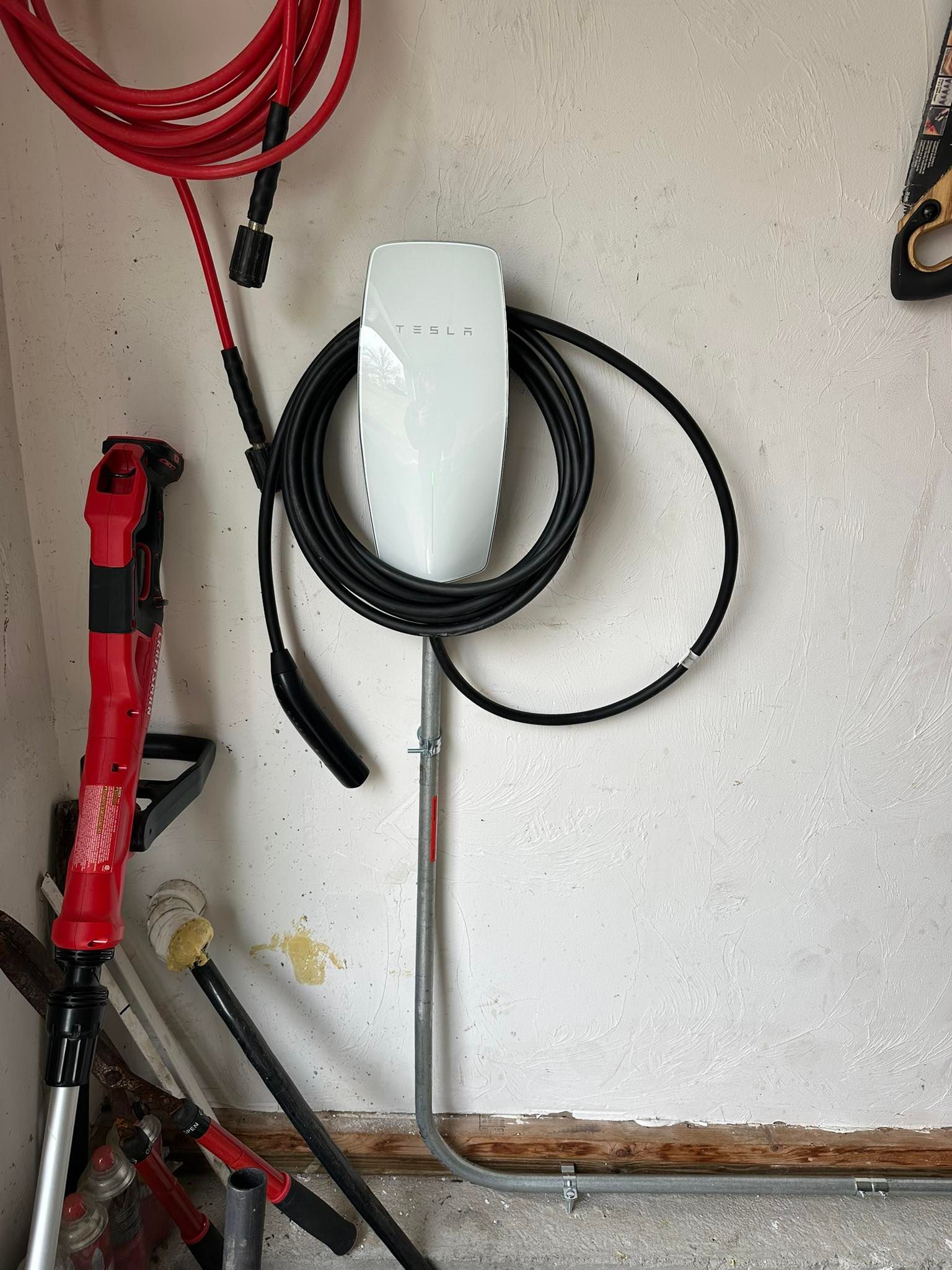 A white Tesla Wall Connector mounted on a garage wall with its black charging cable coiled around it.