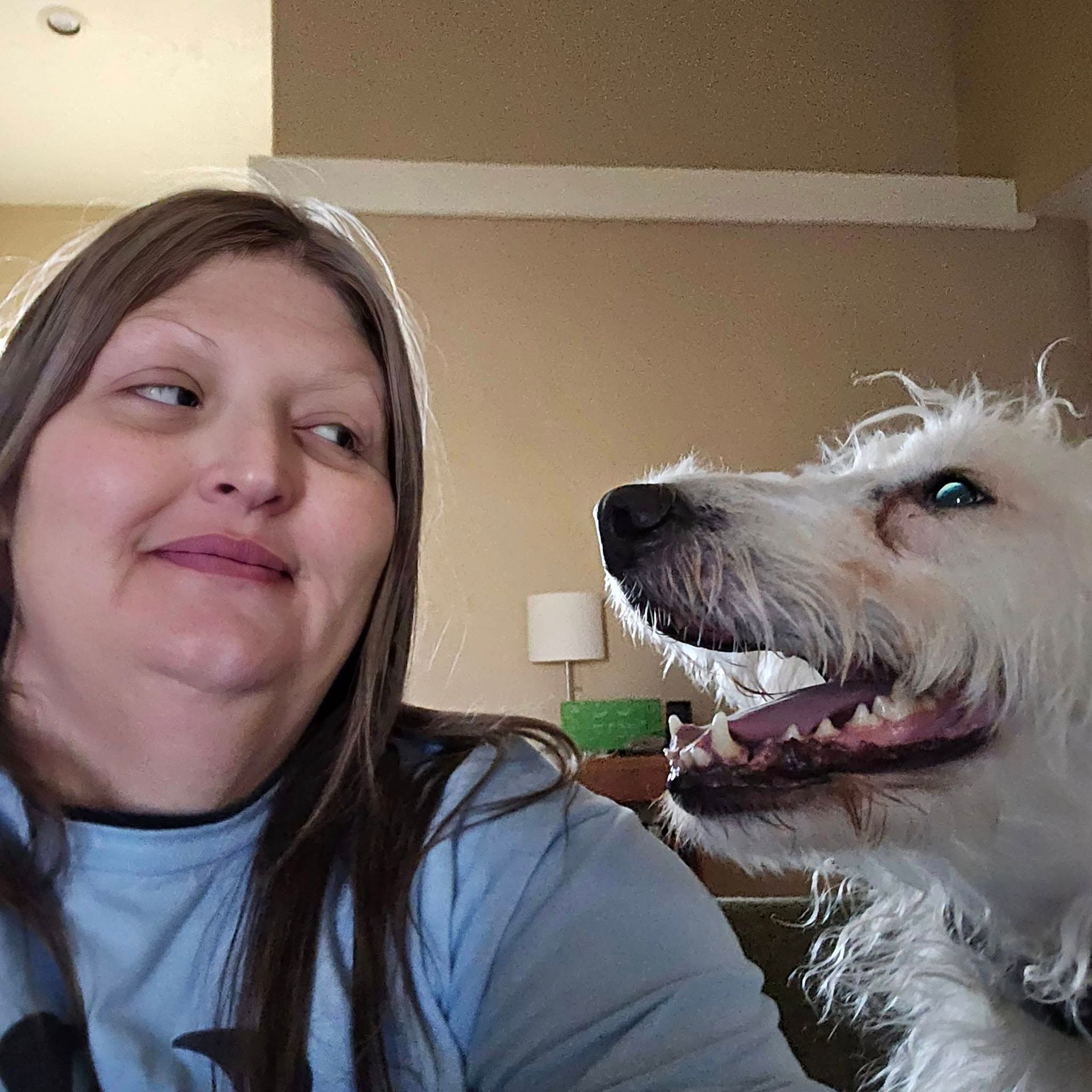 Woman smiles, looking left; shaggy white dog with open mouth to her right.