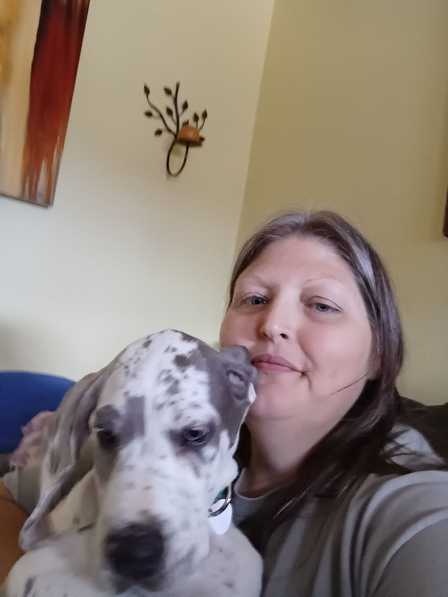 Woman with a Great Dane puppy, both close-up and smiling. The puppy has blue and white spots, resting on her shoulder.
