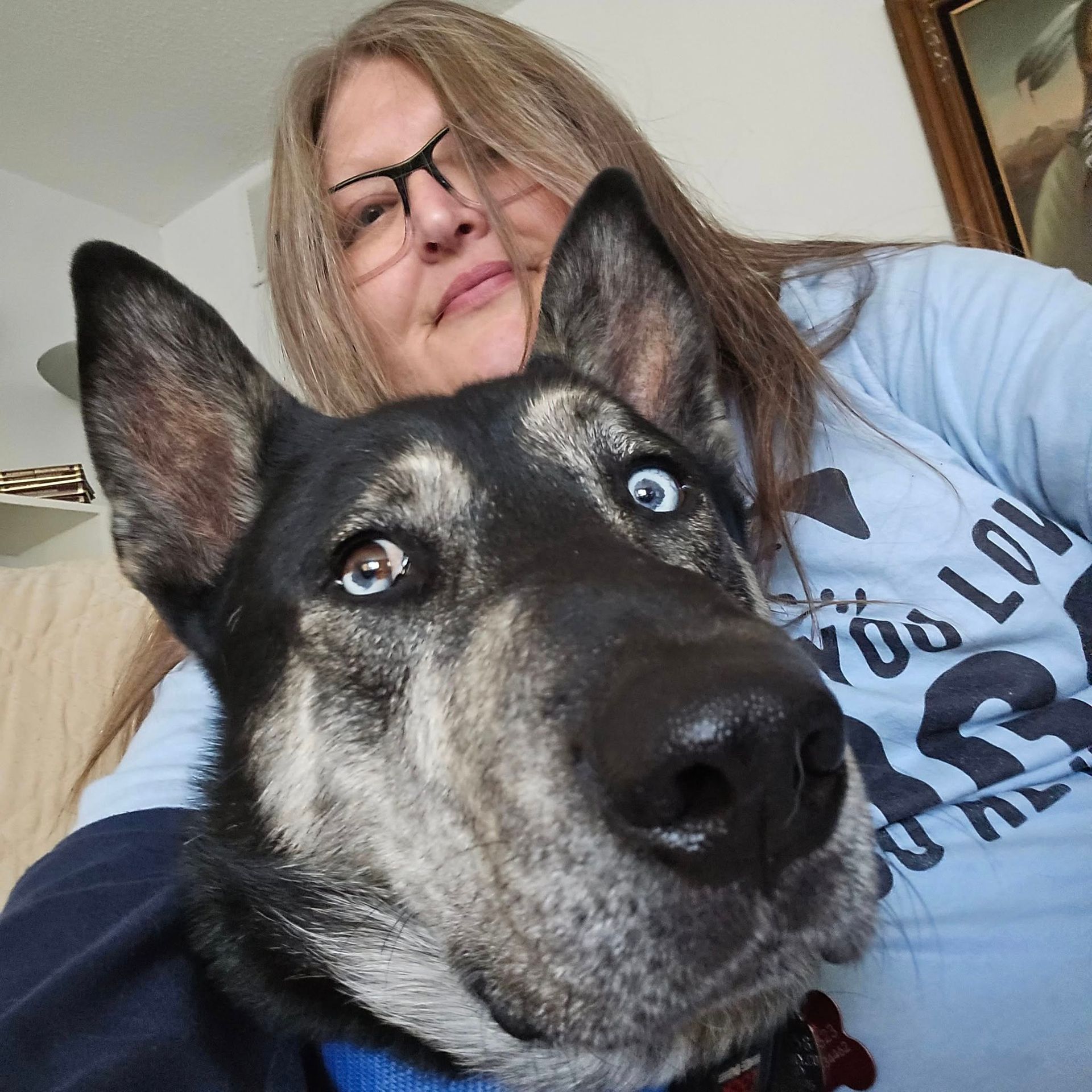 Woman with glasses and husky dog with one blue eye, both looking at the camera.