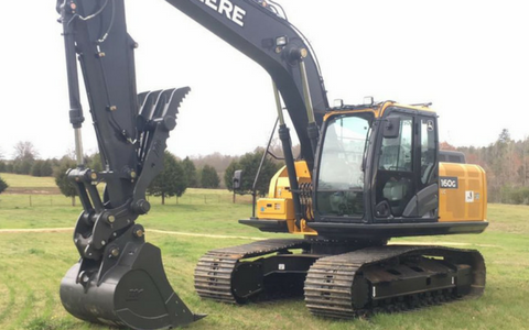 Yellow excavator on tracks with raised bucket in a grassy field under cloudy sky