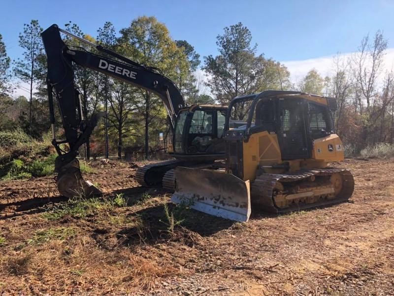 John Deere excavator and bulldozer parked on a dirt clearing beside pine trees