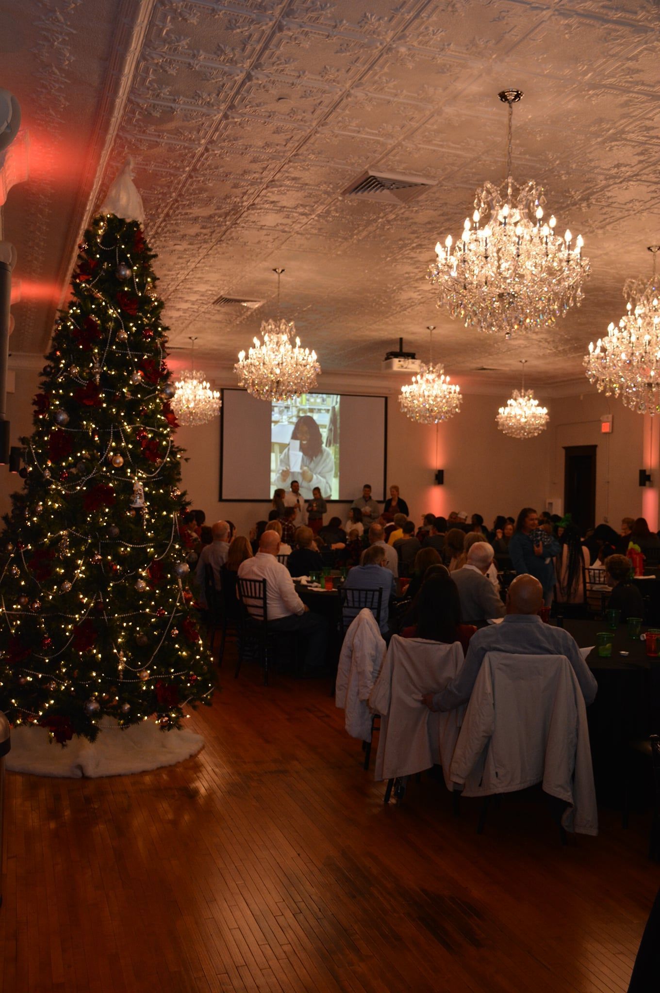 A large room filled with people sitting at tables and a christmas tree.