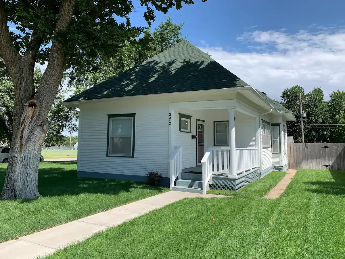 A small white house with a green roof and a porch