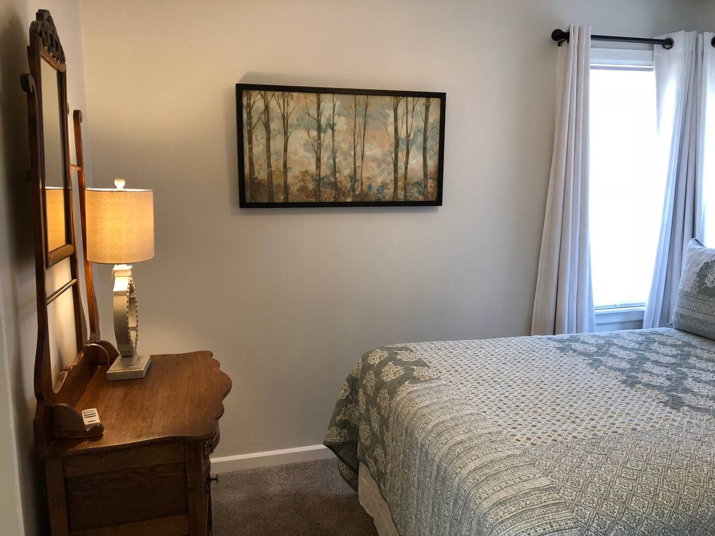 A bedroom with a bed , nightstand , mirror and lamp.