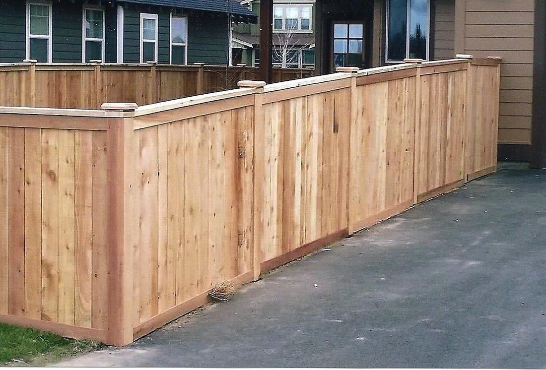 Wooden fence curving along asphalt, beside a building and grass.