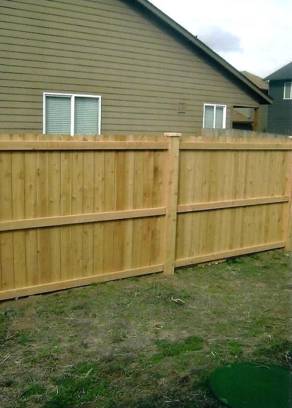 Wooden fence in front of a house, set in a grassy yard.