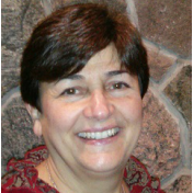 A woman is smiling in front of a stone wall.