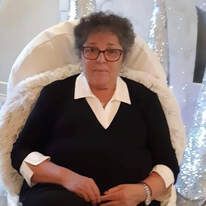 An elderly woman wearing glasses is sitting in a chair.