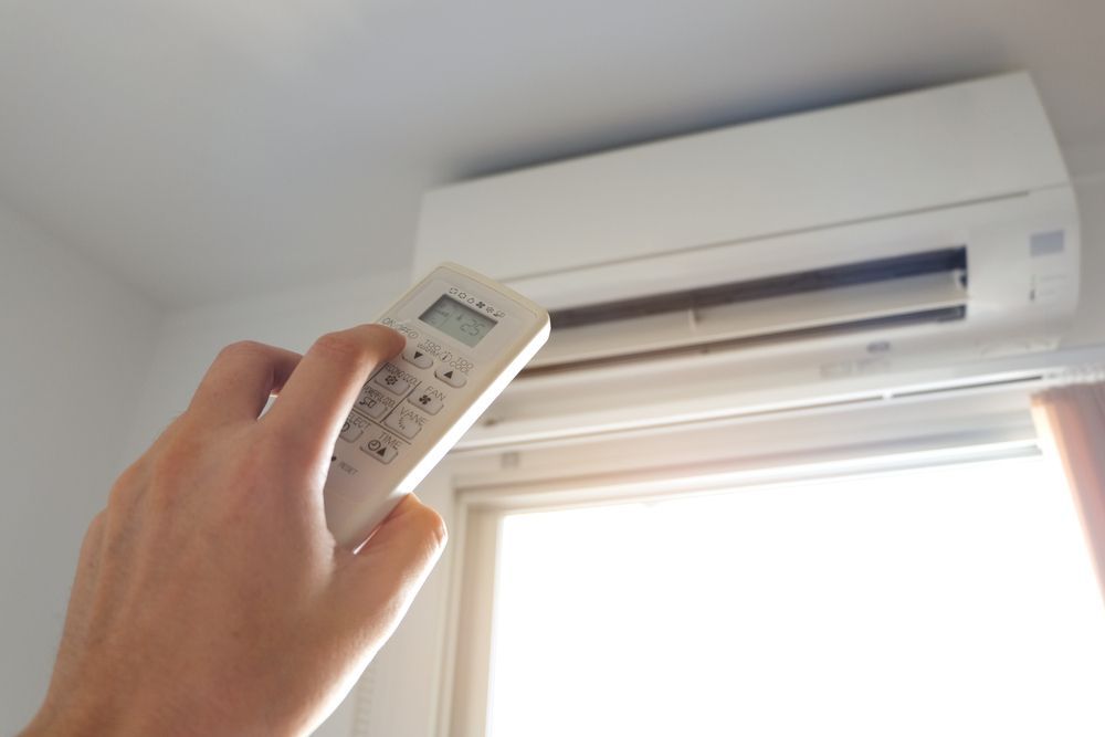 A Person is Holding a Remote Control in Front of an Air Conditioner — Jhe Air Conditioning Services in Saratoga, NSW