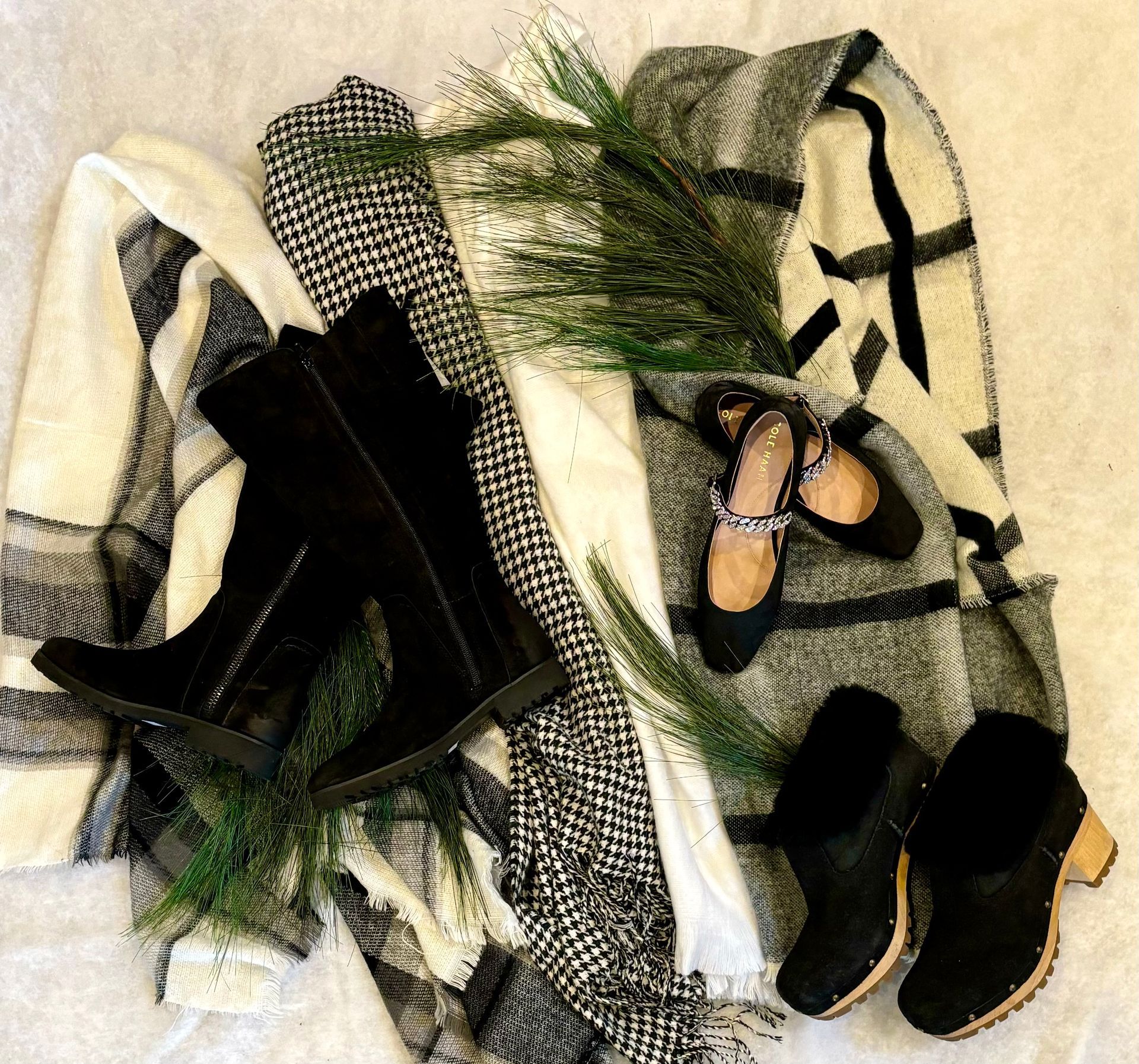 A sweater , scarf , boots , and shoes are laying on a bed.