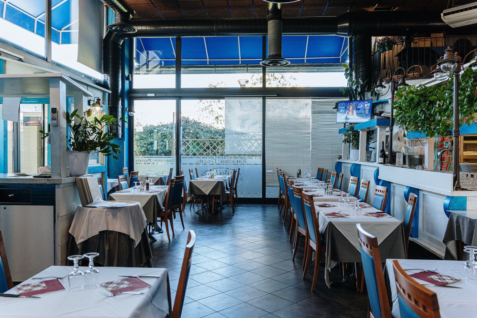 Interno del ristorante con tavoli, sedie e grandi finestre, caratterizzato da una combinazione di colori blu e bianco.