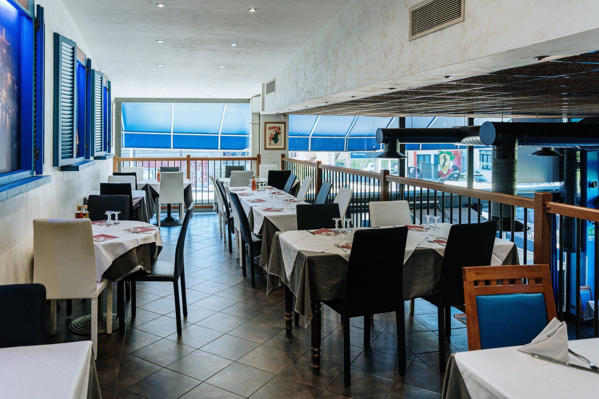Interno del ristorante con tavoli apparecchiati per cenare, finestre con vista e decorazioni blu e bianche.