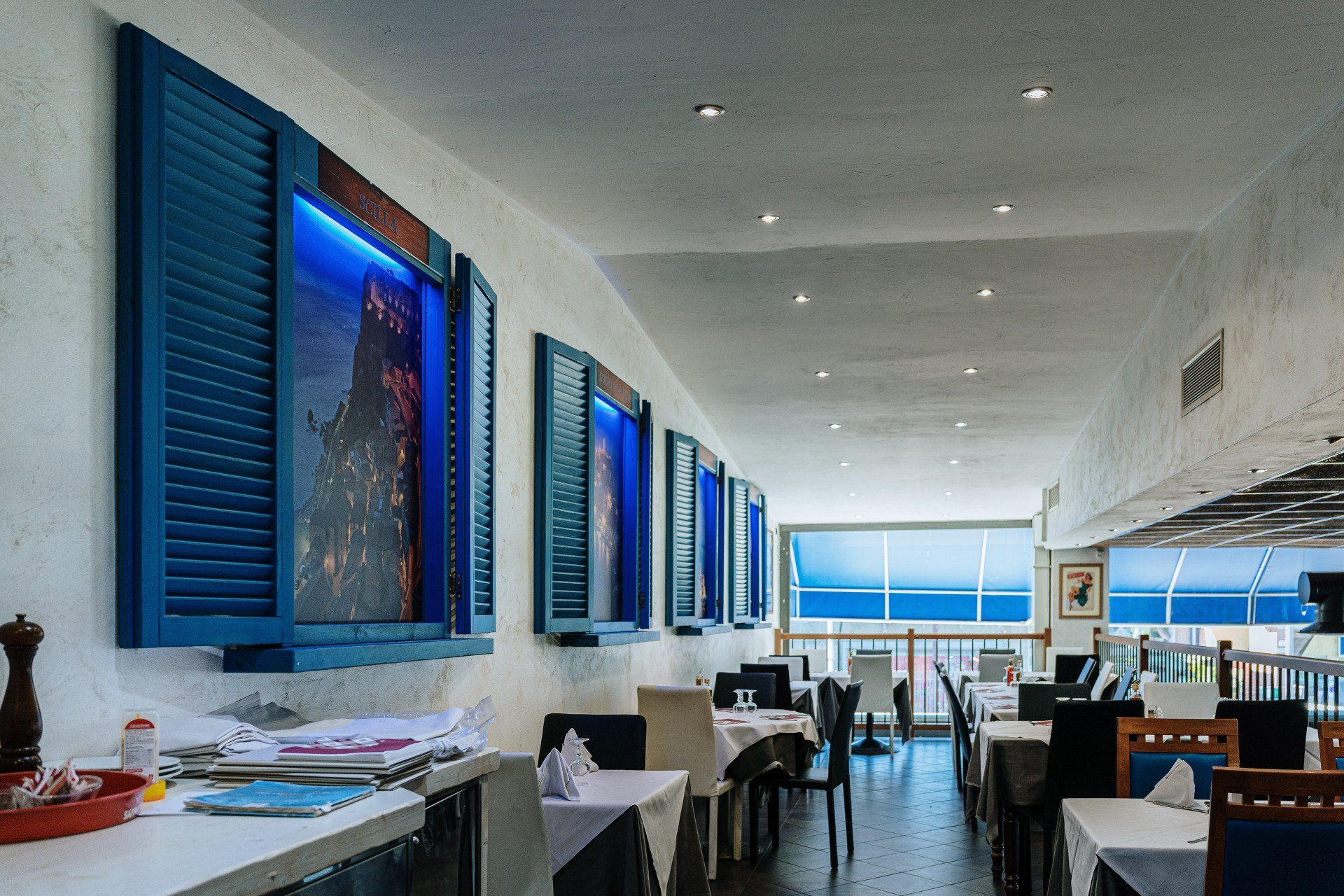 Interno del ristorante con pareti bianche, persiane blu e tavoli apparecchiati per mangiare.