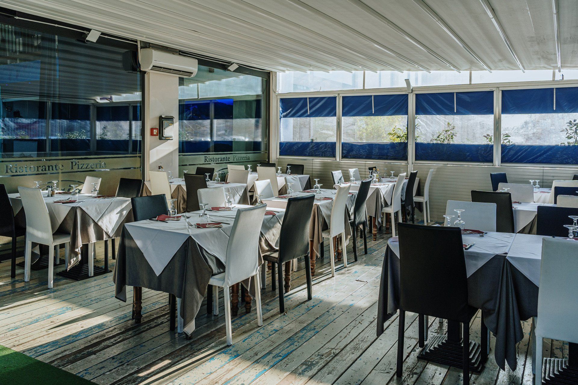 Sala da pranzo del ristorante con tavoli apparecchiati per gli ospiti, colori bianco e grigio, sotto un tetto retrattile.