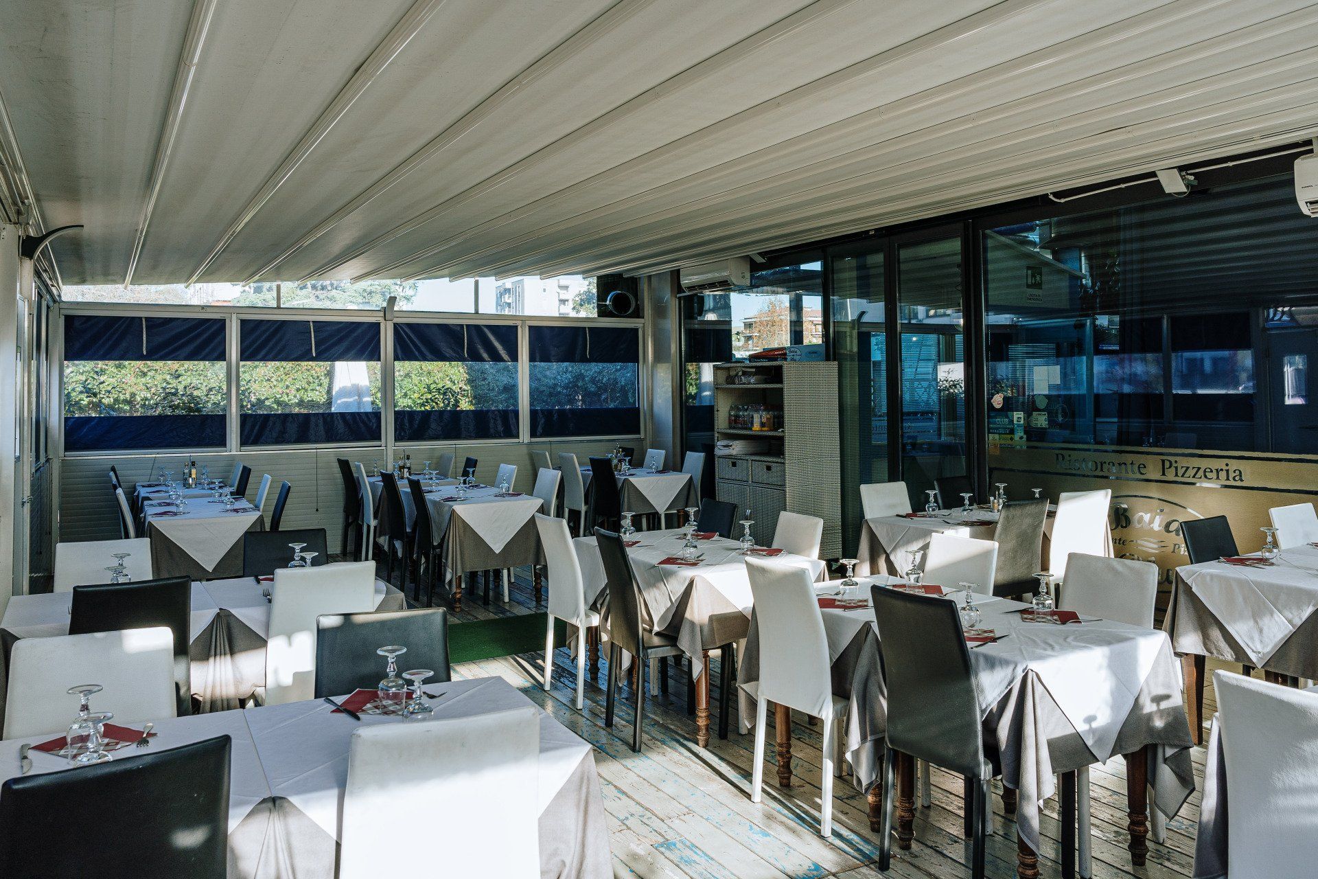 Patio del ristorante: tavoli apparecchiati per i commensali, sotto un tetto retrattile, con finestre e luce che filtra all'interno.