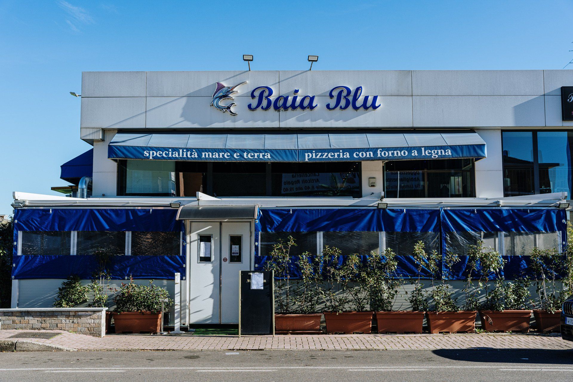 Ristorante Baia Blu con tenda blu e insegna in una giornata di sole.