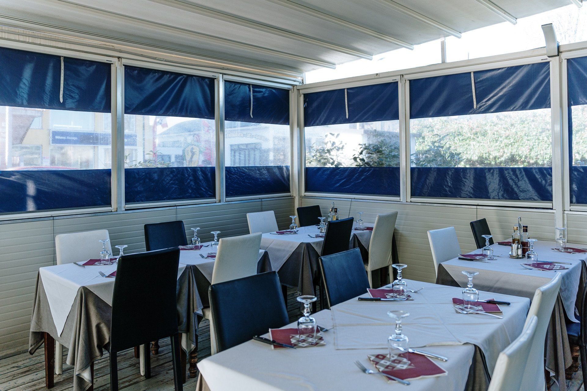 Sala da pranzo del ristorante con tavoli apparecchiati per i pasti, tende blu e tovaglie bianche.