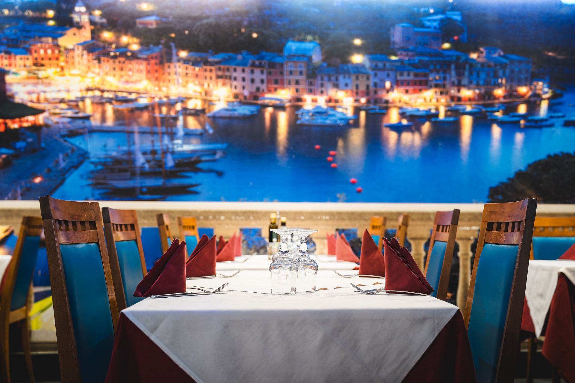 Tavolo del ristorante apparecchiato con bicchieri e tovaglioli, con vista sul porto e sulle luci della città.