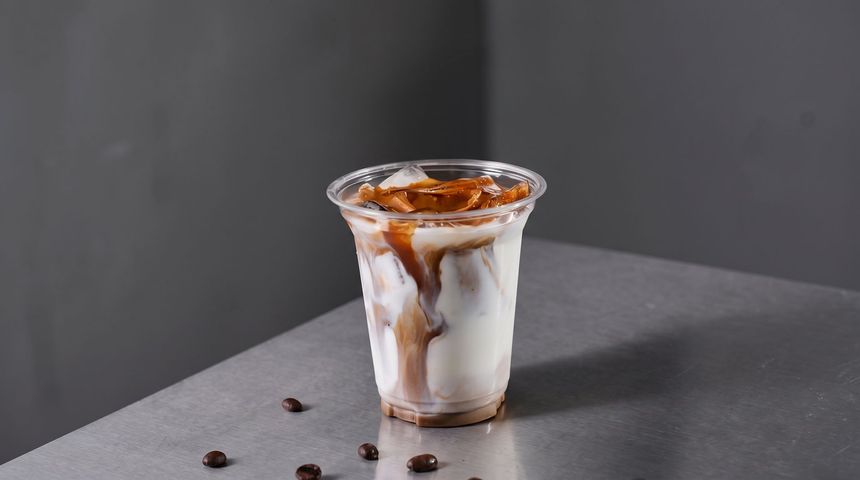 Glass of iced coffee with caramel drizzle on a gray tabletop, with coffee beans nearby