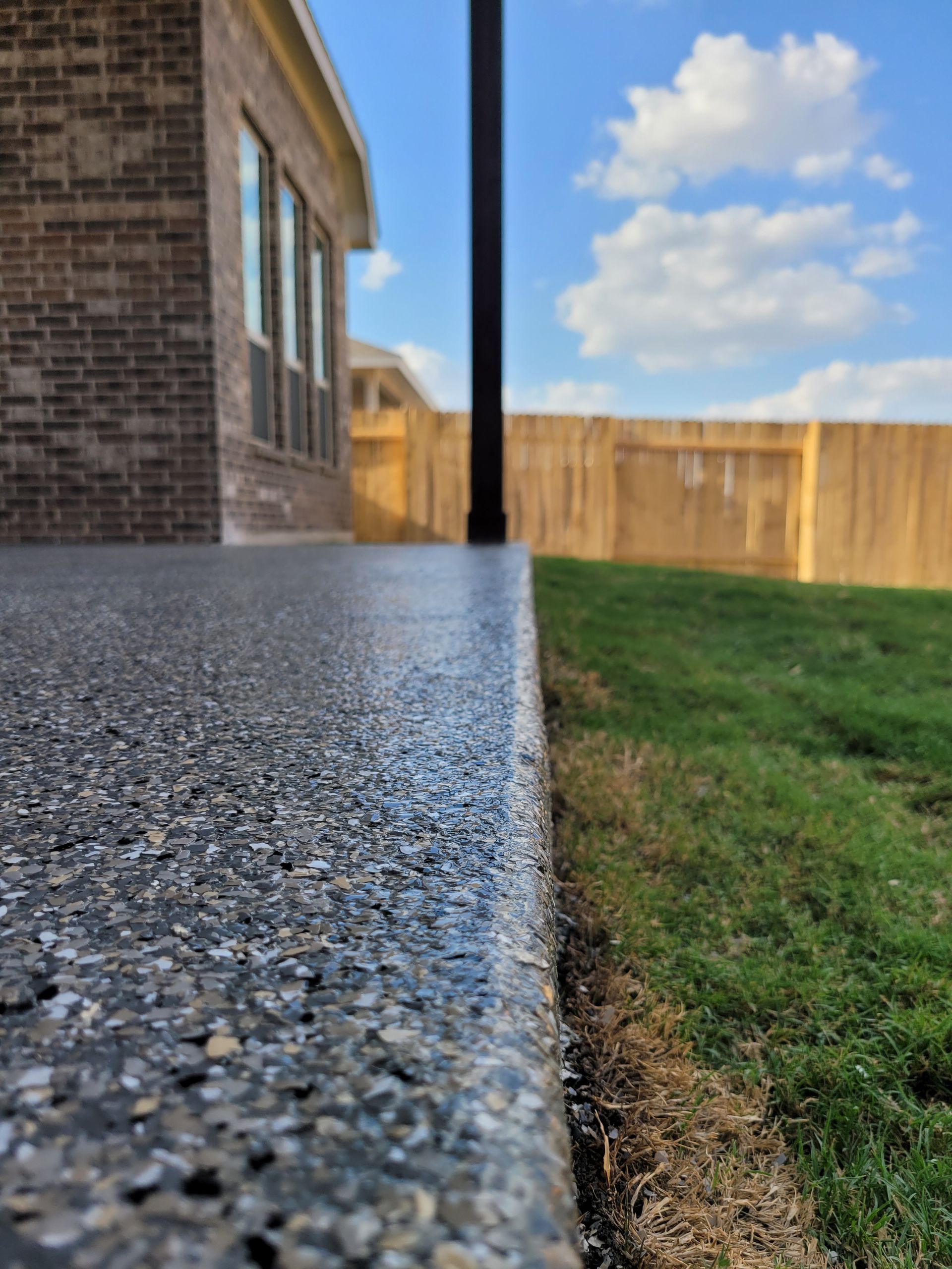 a brick house with a fence in the background and a concrete walkway in the foreground .