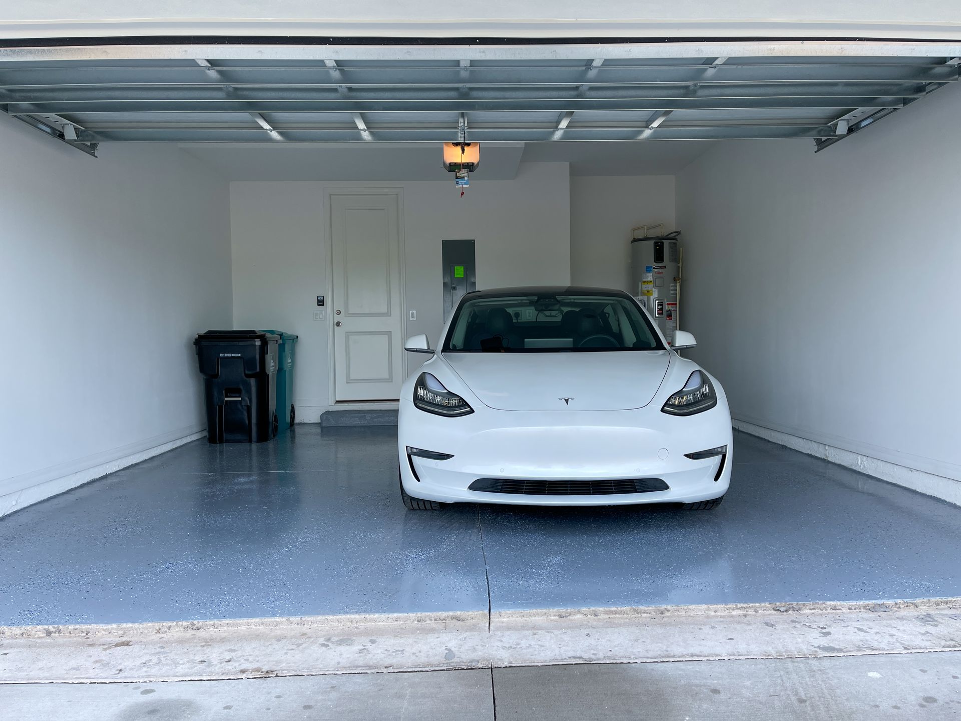 a white tesla model 3 is parked in a garage with its door open .