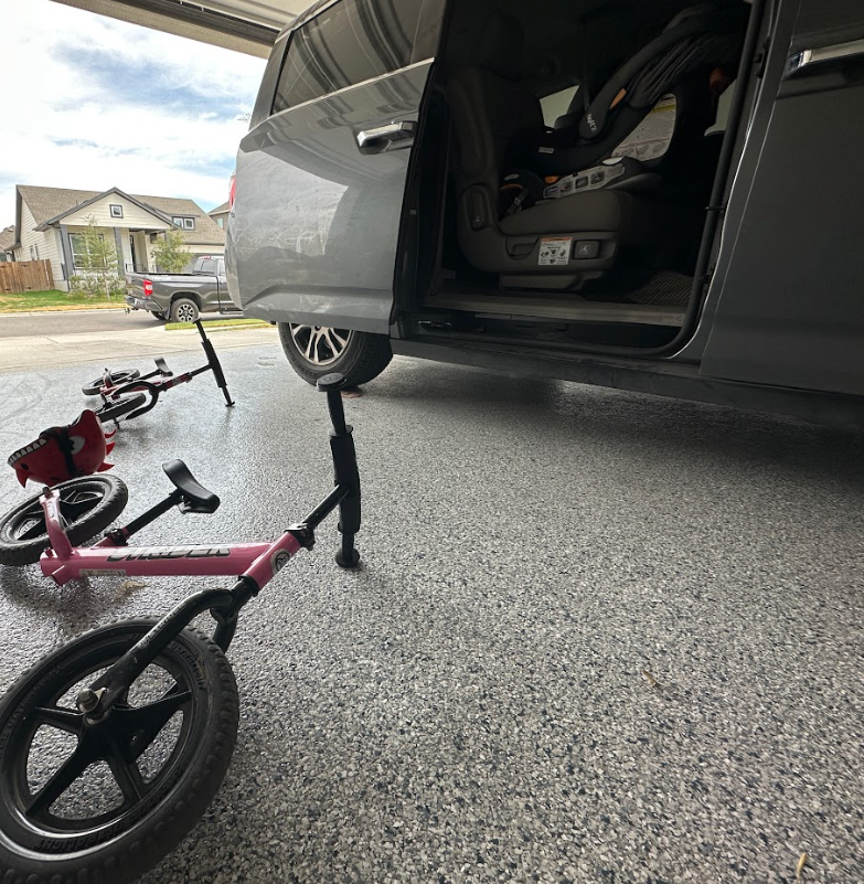 a pink balance bike is parked next to a gray van in a garage.