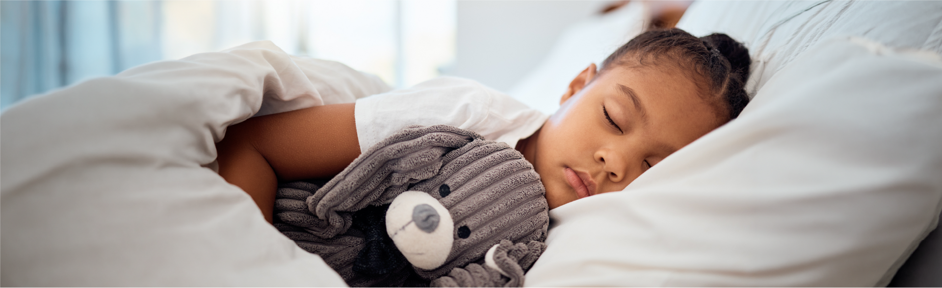 A child sleeping peacefully in bed while hugging a gray stuffed animal.