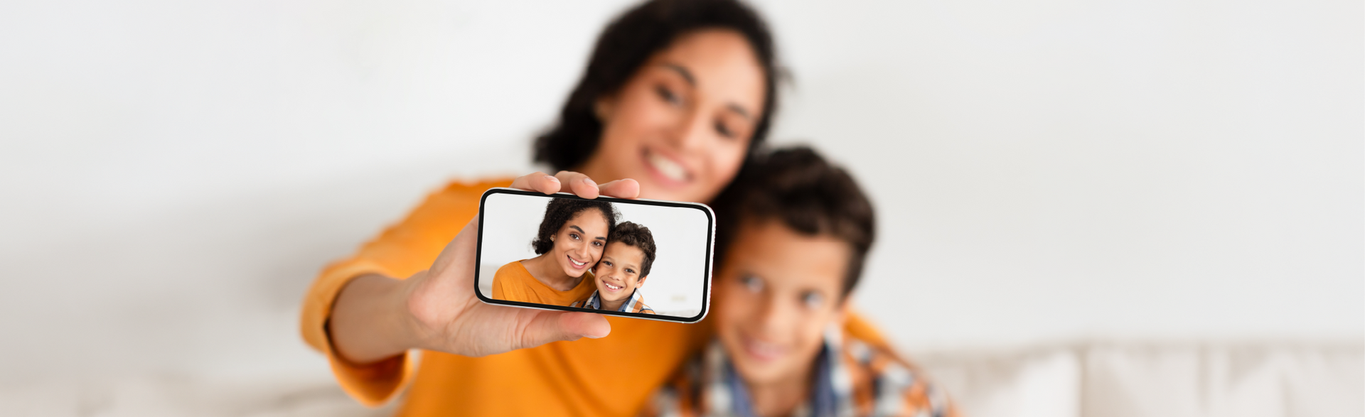 A smiling parent and child take a selfie together while sitting indoors.