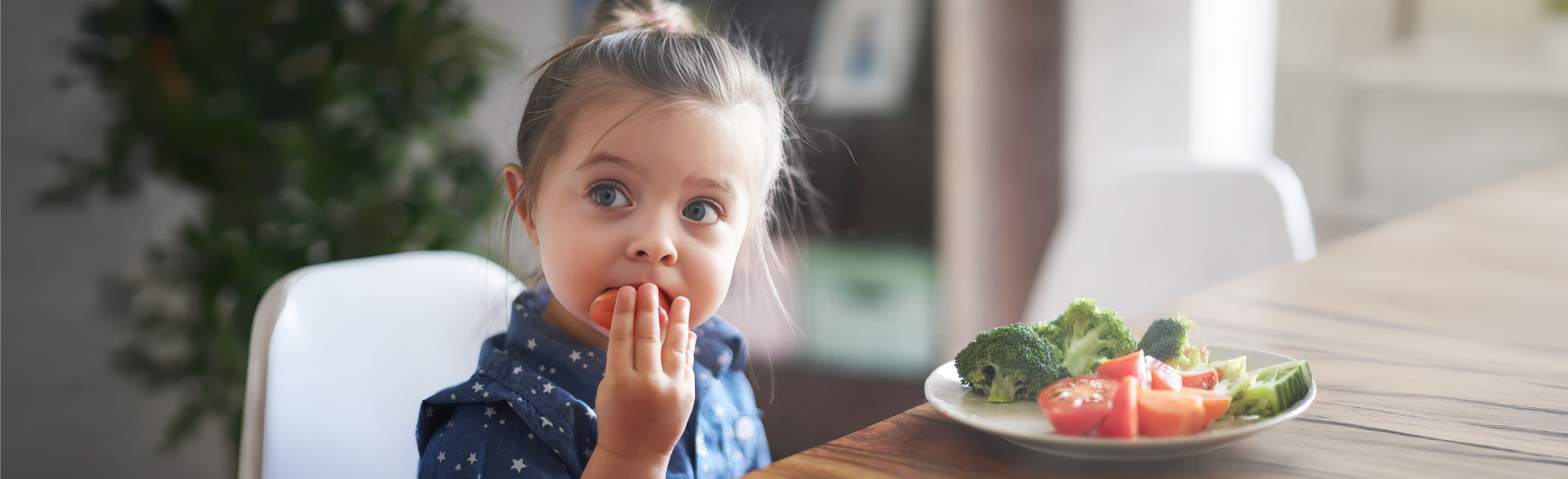A young child eats vegetables from a plate at a dining table.