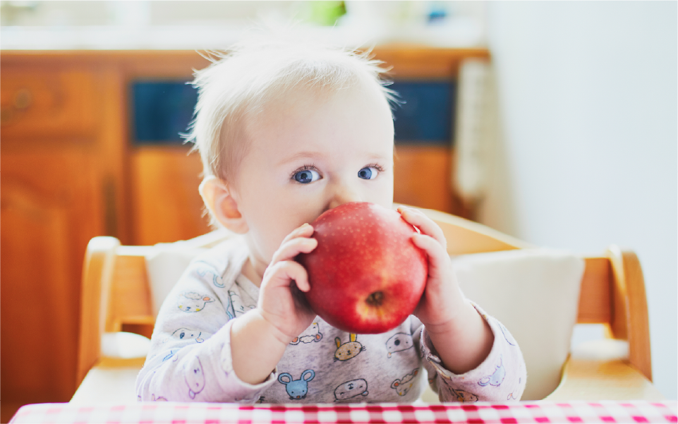Baby being fed with a spoon, wearing a white bib and looking up with mouth open.