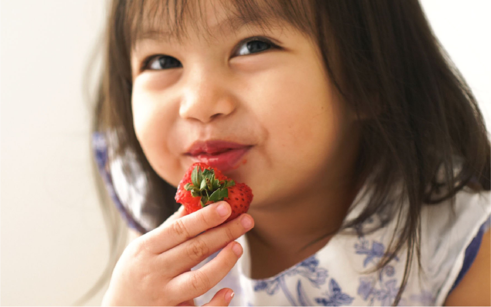 Baby being fed with a spoon, wearing a white bib and looking up with mouth open.