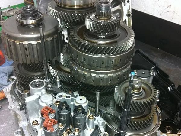 Disassembled transmission components: gears, drums, and solenoids, on a workbench.