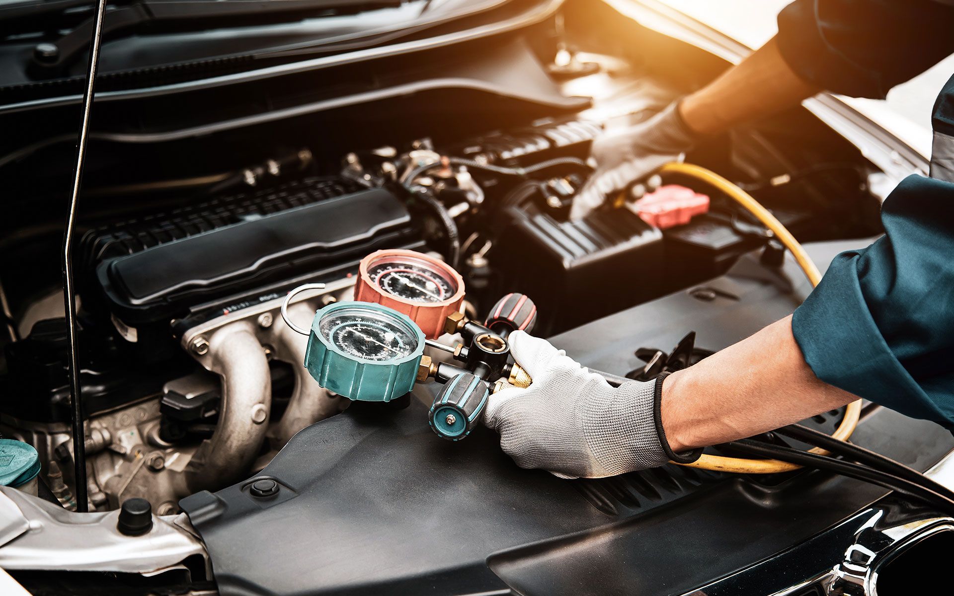 Mechanic working on a car engine with gauges attached.