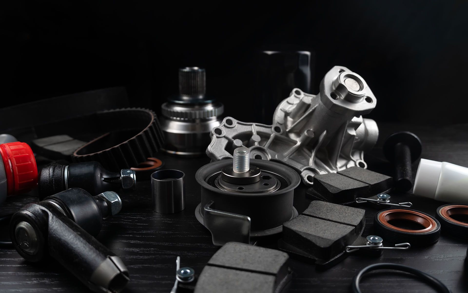Car parts scattered on a dark surface, including a water pump, brake pads, and belts.