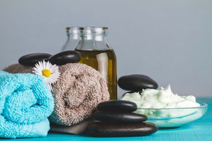 Spa towels, stacked massage stones, bottles of oil, and white lotion on a turquoise surface