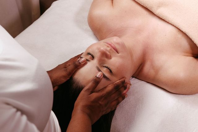 Spa therapist giving a facial massage to a reclining client on a treatment bed
