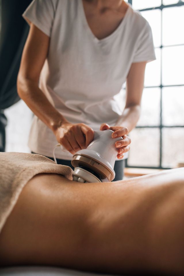 Therapist using a handheld massage device on a client’s back in a bright treatment room