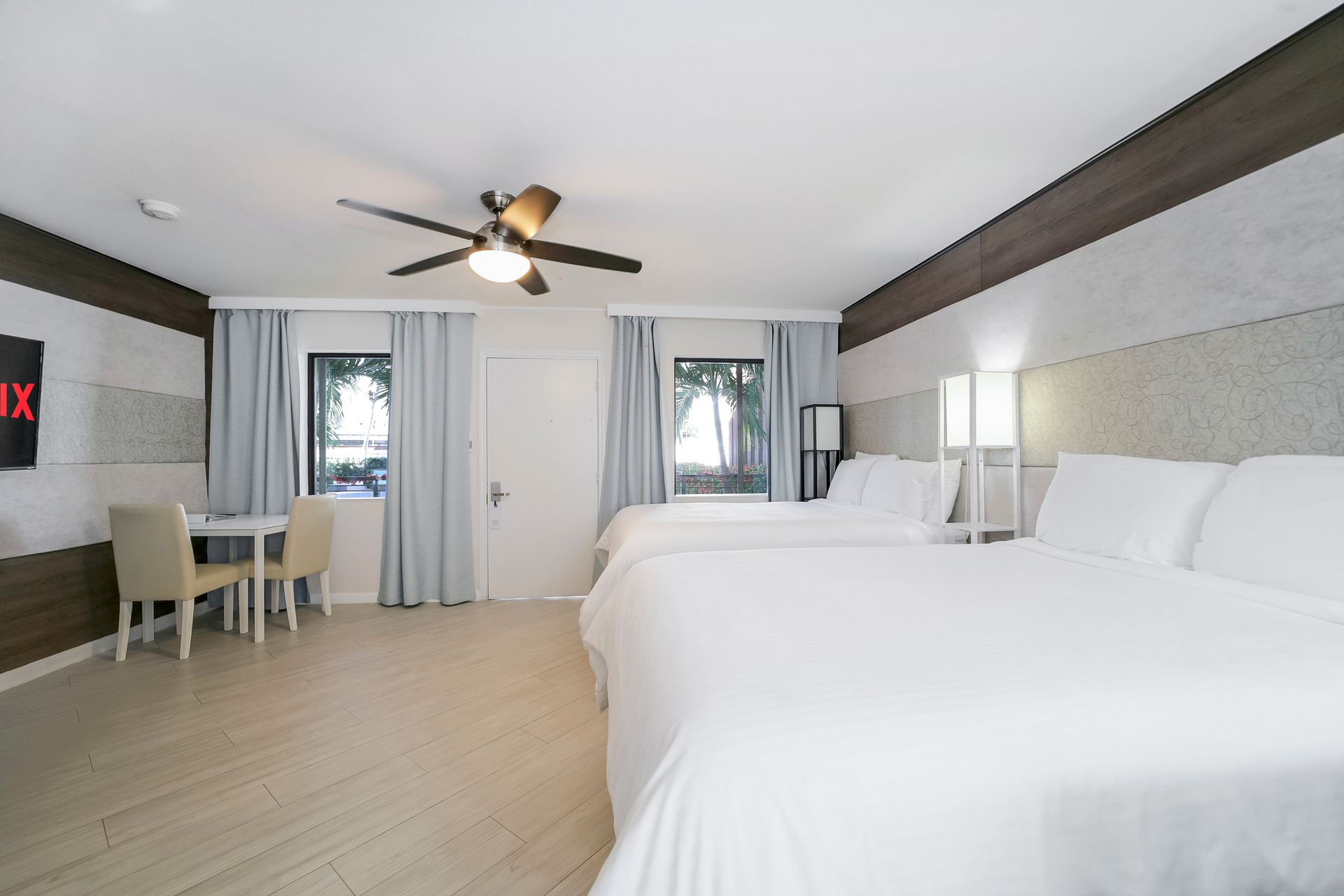 Hotel room with two queen beds, a table with chairs, and a ceiling fan.