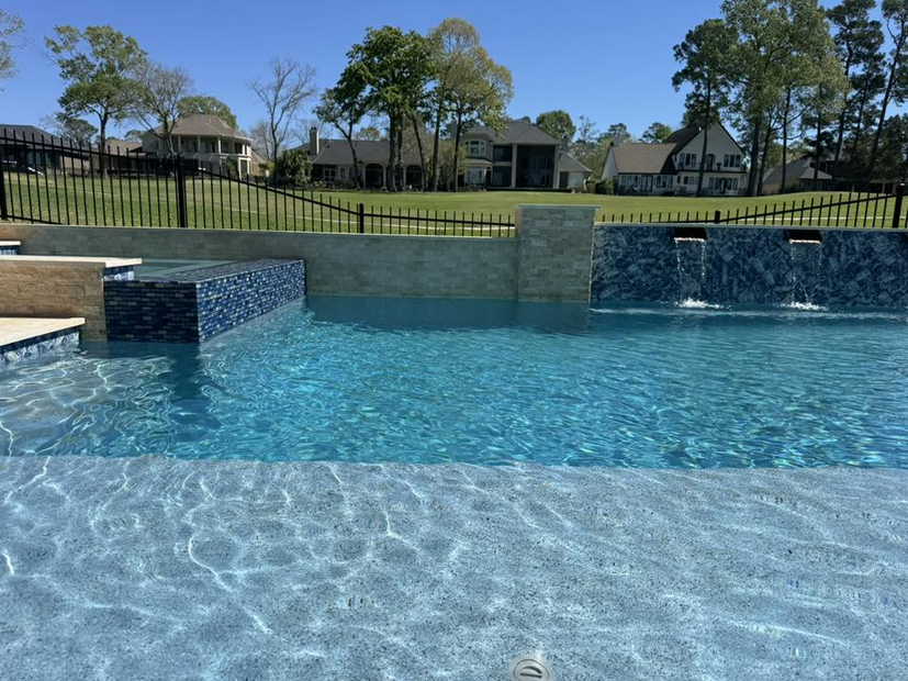 Backyard swimming pool with blue water, stone waterfall walls, and houses in the background