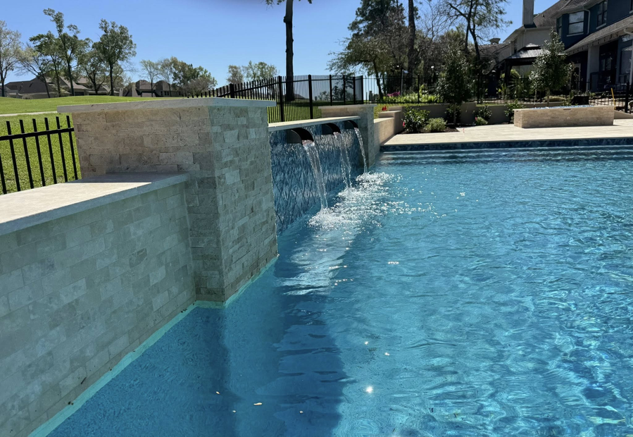 Backyard swimming pool with blue water, stone waterfall walls, and houses in the background