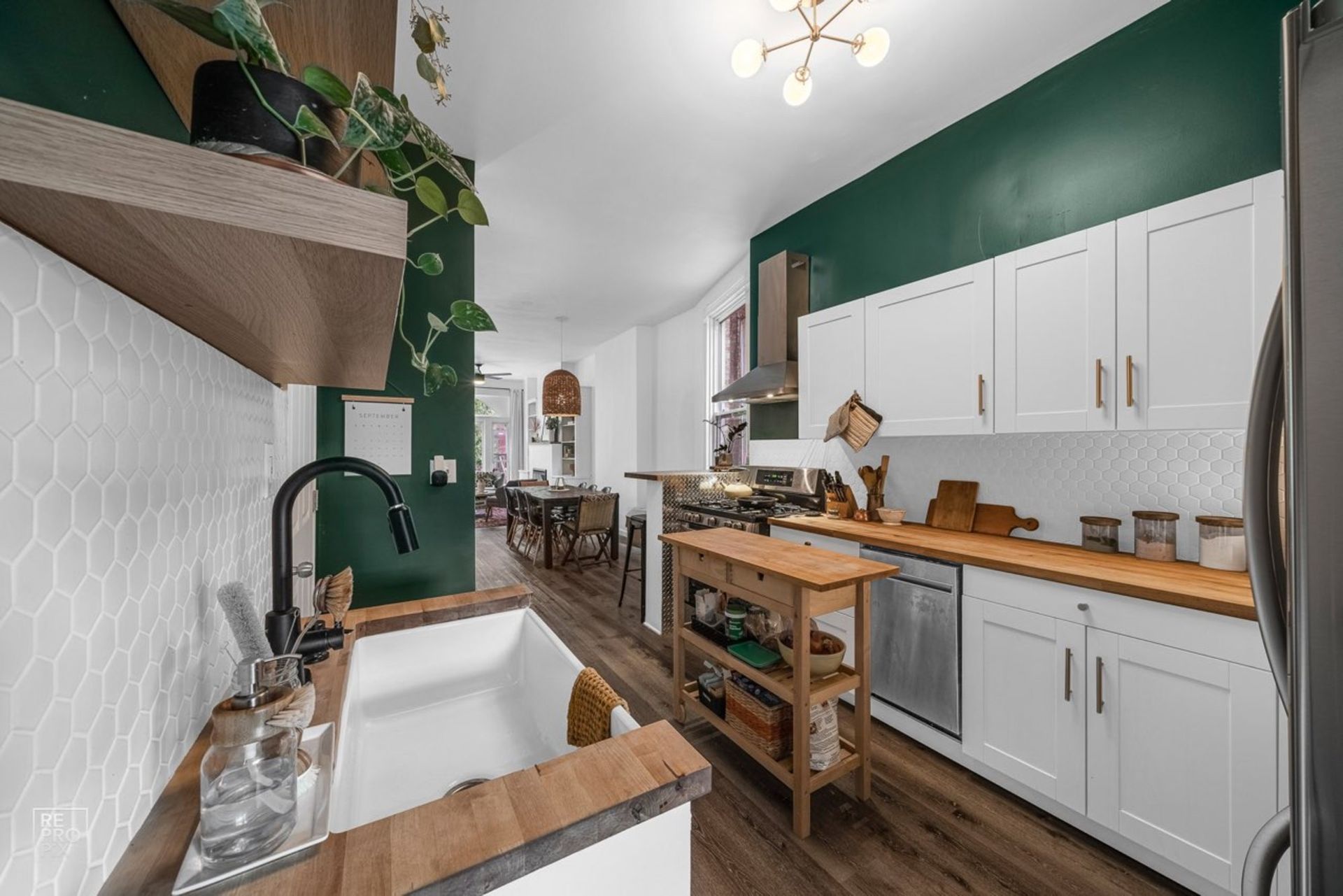 A kitchen with white cabinets , wooden counter tops , a sink and a refrigerator.