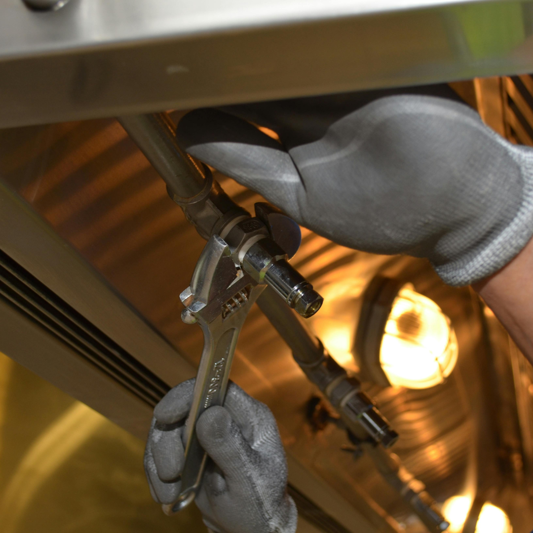 A person wearing gloves is working on a pipe with a wrench