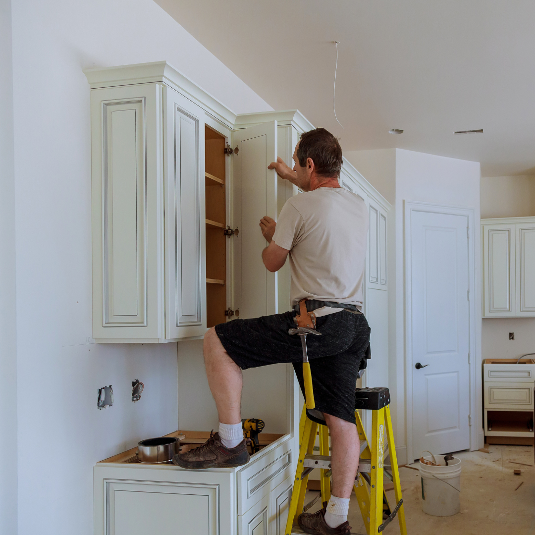 A man standing on a ladder working on a cabinet